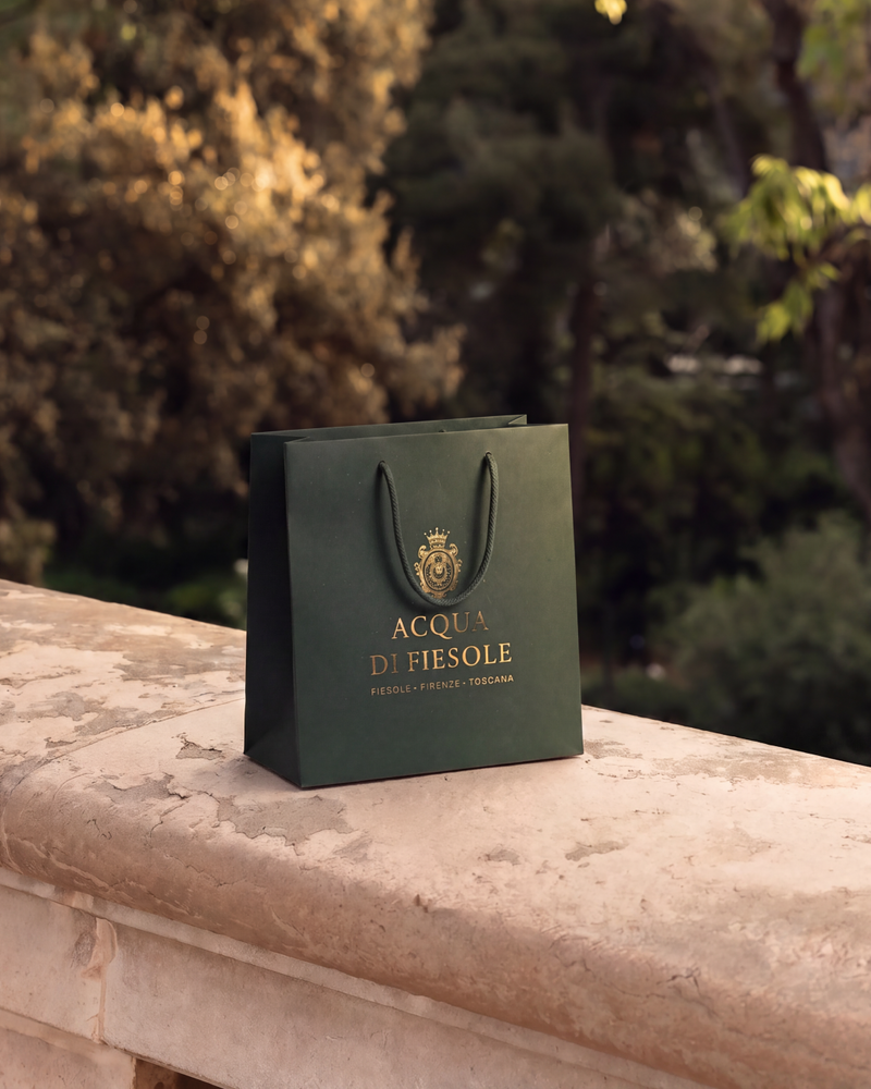 Shopper verde con logo dorato su un muretto in pietra nel giardino